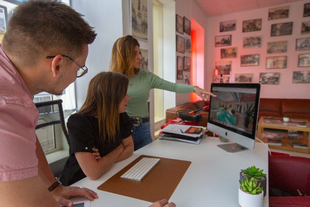 3 agents RESIDE immobilier discutent autour d'un bureau, l'un désigne sur un écran d'Imac, un bien vendu à Amilly